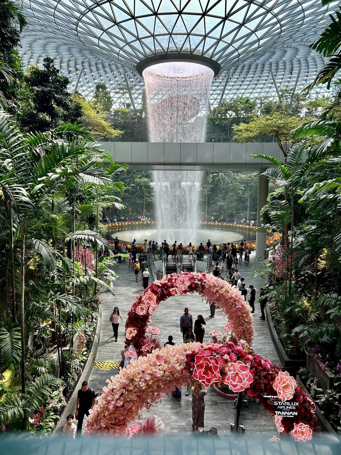 The Rain Vortex at Jewel Changi framed by a pink floral arch installation on the garden walkway